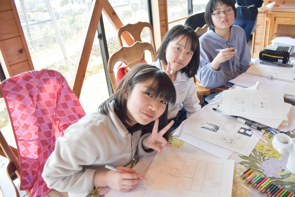 Children sitting at a table drawing comics with pencils and markers in a bright room. - group activity in an art class