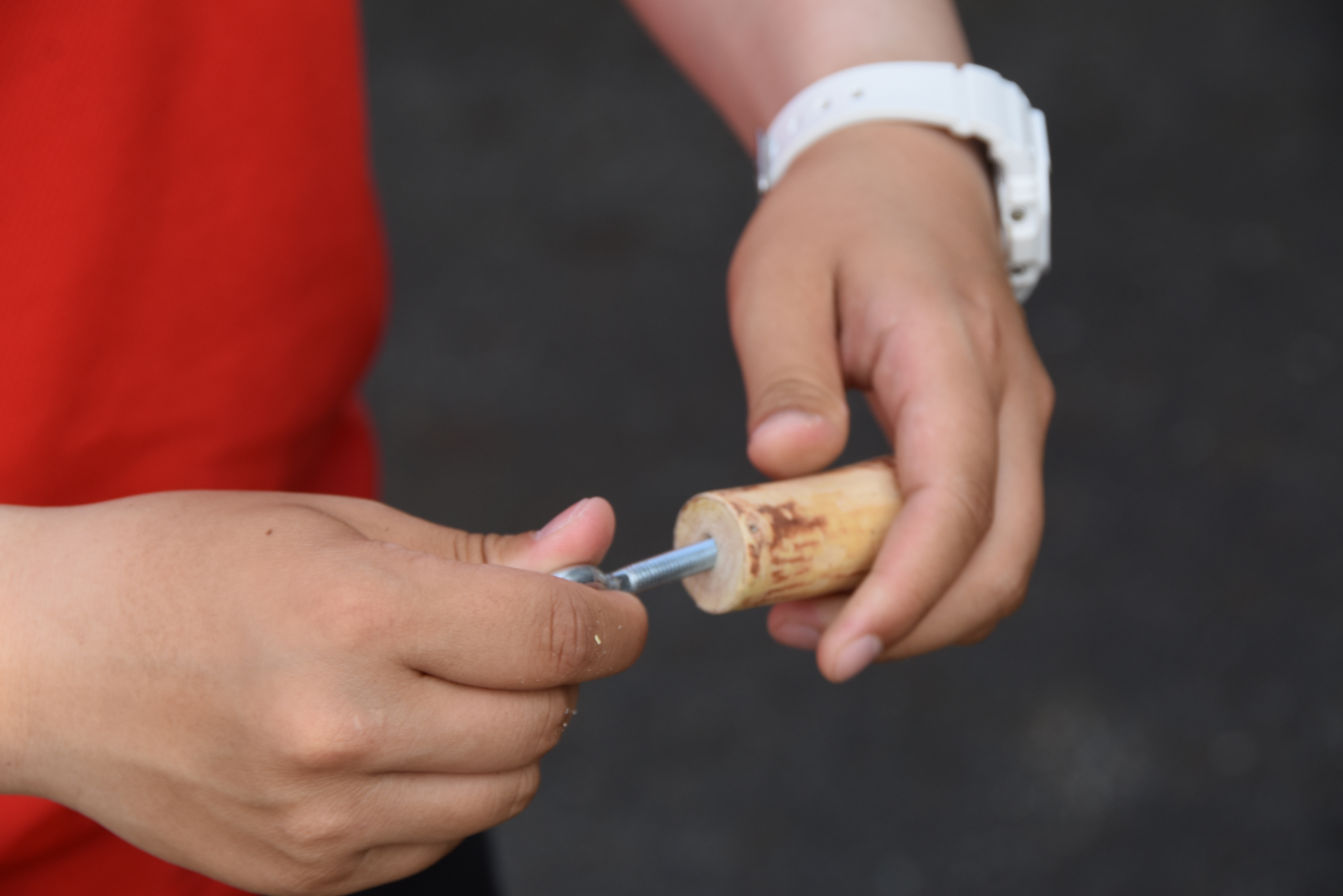 Close-up of two hands holding a wooden-handled tool and a metal rod, with a white watch visible on the wrist.