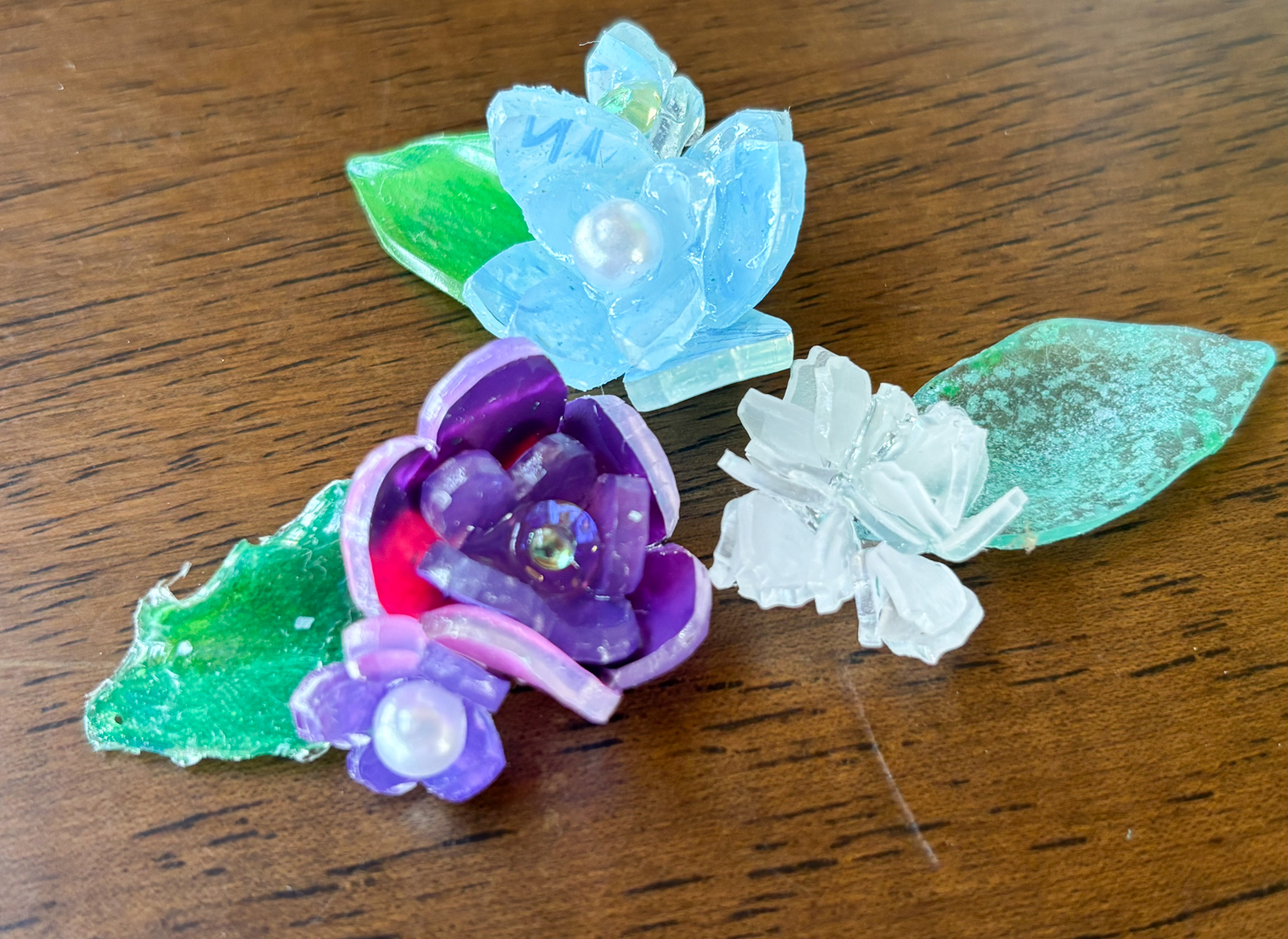Colorful translucent flower shapes (blue, purple, white) with green leaves on a wooden surface.