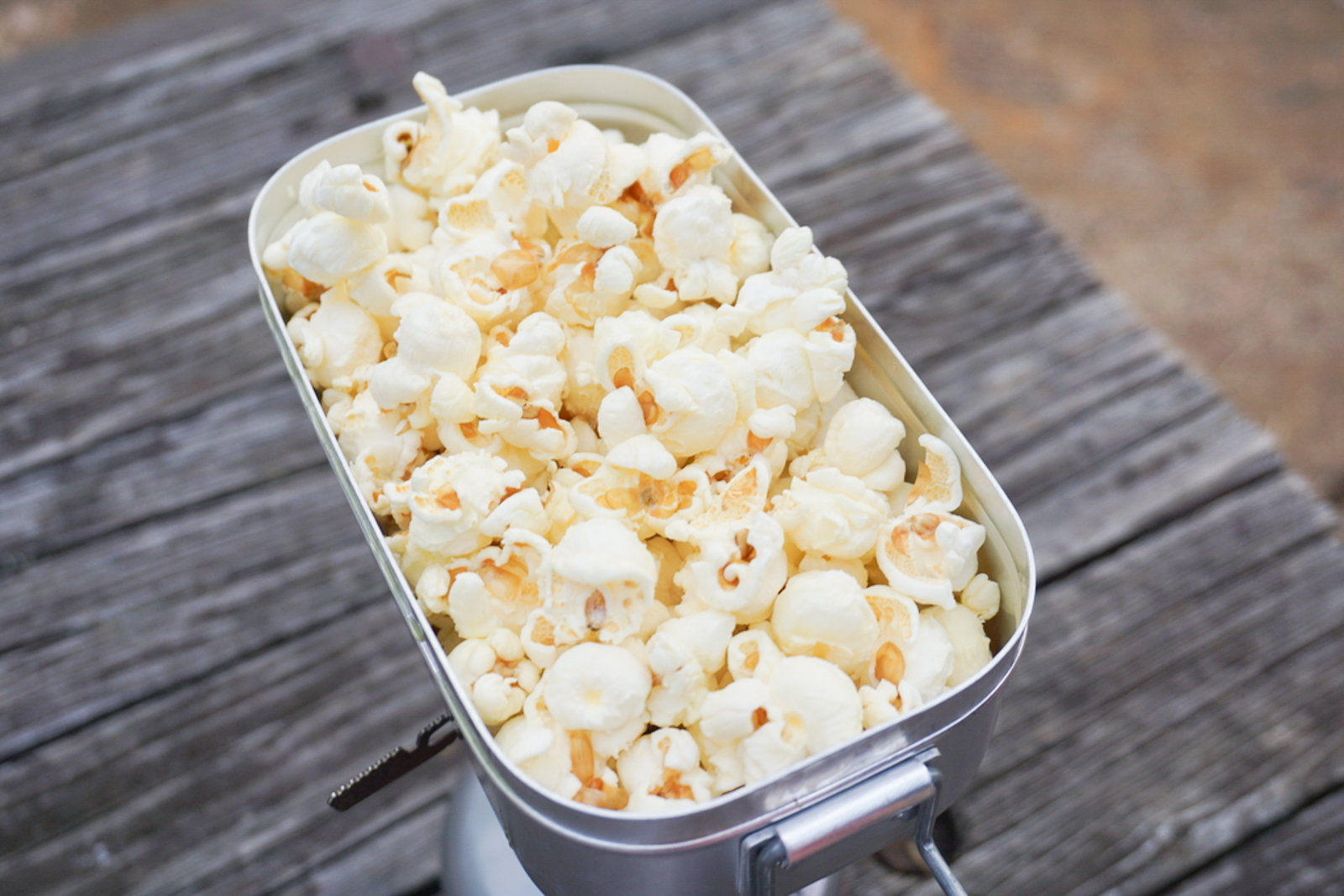 Tin of popcorn filled with fluffy white kernels on a weathered wooden surface seen from above/side angle